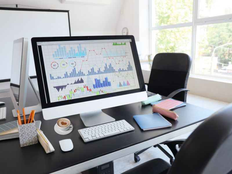 Organizacija radnog prostora u modernoj kancelariji sa računarom na kojem su prikazani grafici i analitički podaci, uredno okruženje sa sveskama i šoljicom kafe.