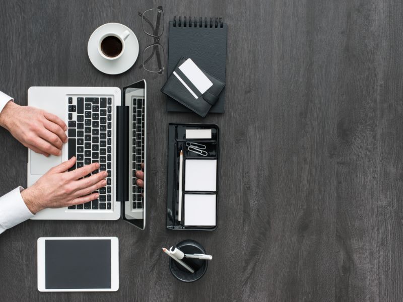 Organizacija radnog prostora prikazana odozgo, sa laptopom, tabletom, šoljicom kafe i uredno raspoređenim kancelarijskim priborom na tamnom stolu.