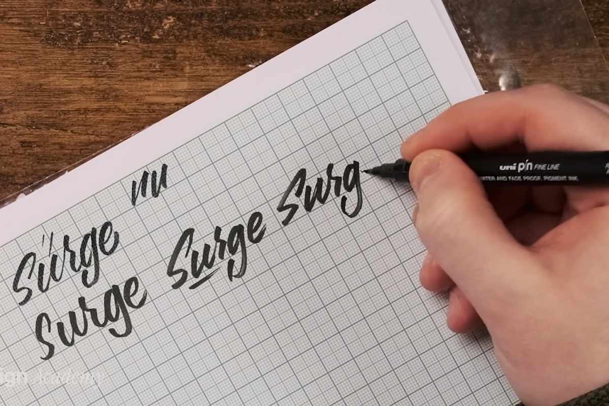 Ruka drži crni marker i ispisuje reč na papiru sa kvadratnom mrežom, prikaz vežbanja tipografije i kaligrafije